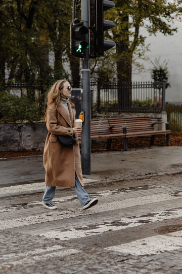 Femme marchant dans la lumière d’automne, boisson chaude à la main.