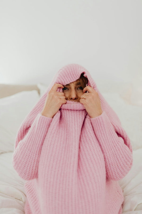 Femme emmitouflée dans un pull chaud sur son lit