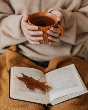 Femme détendue sous un plaid avec une tasse de thé, ambiance cocooning automnale